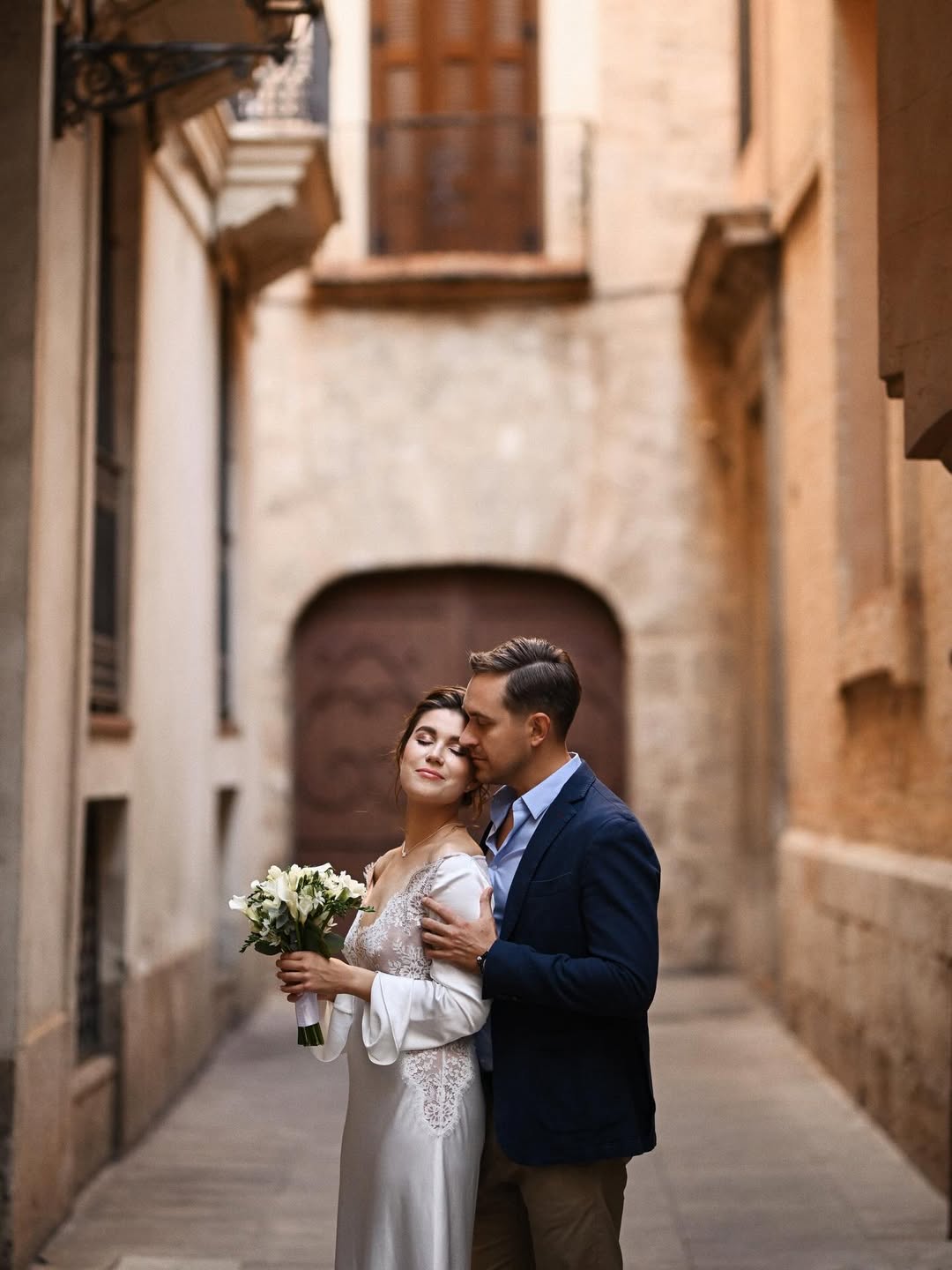 A refined portrait of a couple framed by the ornate stone archways of Valencia's historic center. High-end wedding photography showcasing local heritage and elegance